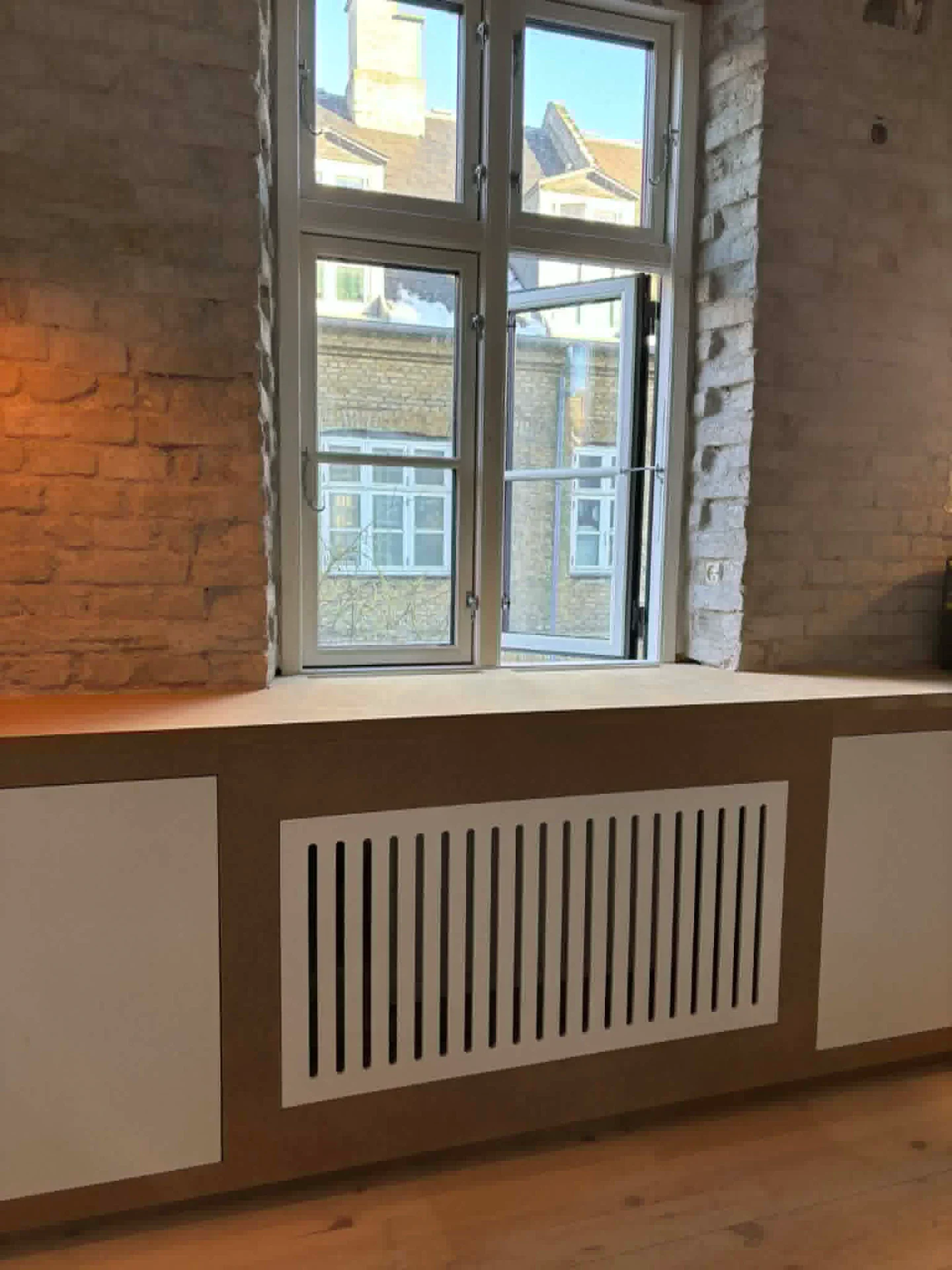 Vindueskarm med radiatordække under et stort vindue i et indendørs rum.