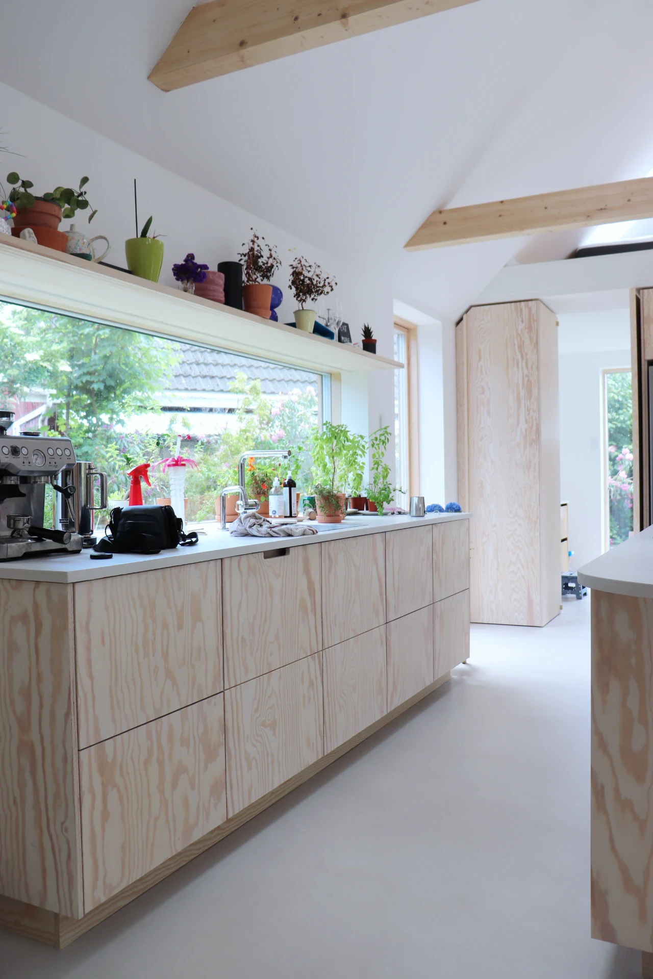 Moderne køkken med træskabe, store vinduer og planter, lyst og luftigt design.